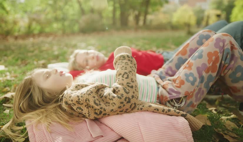 Two carefree young girls relax together on the grass in a sunlit park on a lovely autumn day