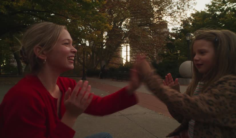 A joyful young woman and a little girl laugh and smile while playing a hand-clapping game together in a park