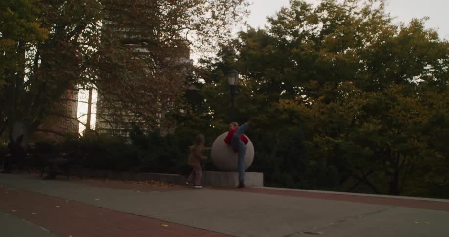 A joyful woman and a young girl chase each other through a city park in an energetic slow-motion clip