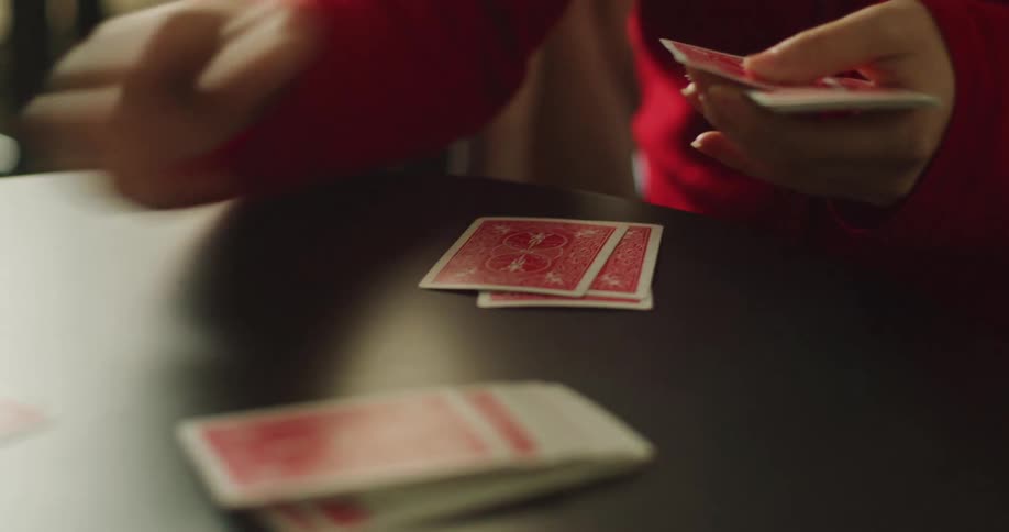 A close-up of hands dealing playing cards face down onto a dark table in preparation for a game