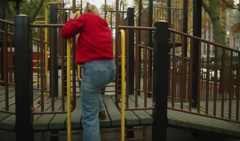 A mother and her young daughter playfully climb on a jungle gym at a city park in slow motion