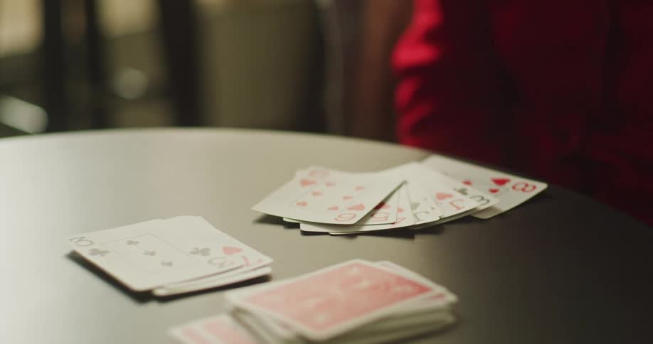 A person in a red sweater lays down their hand of playing cards during a game in a moody, close-up shot