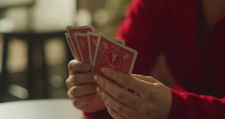 A woman in a red sweater carefully considers her hand before playing a card