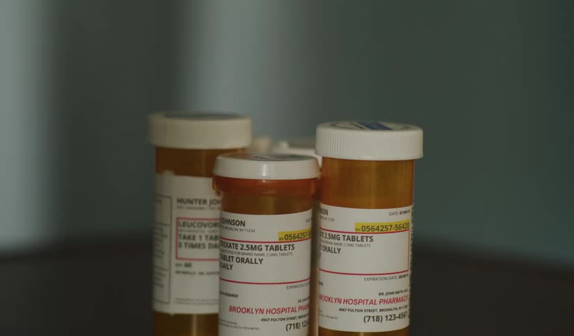 A close-up shot of three prescription pill bottles sitting on a tabletop in a dimly lit room