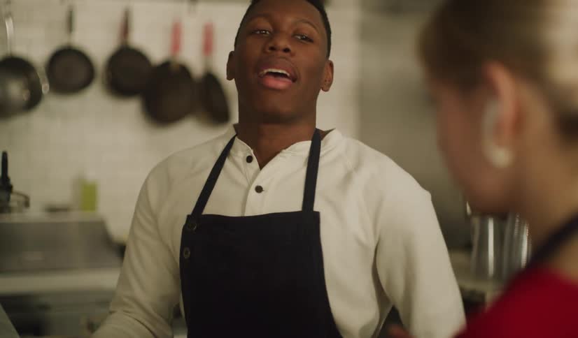 A young African American chef and his female colleague take a break and chat while working in a restaurant kitchen