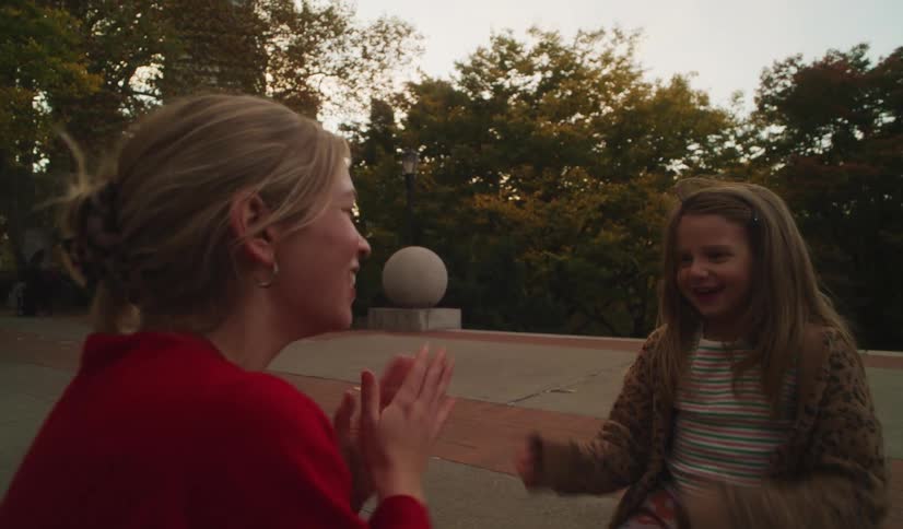 A woman and a young girl share a joyful moment playing a hand-clapping game in a city park in slow motion