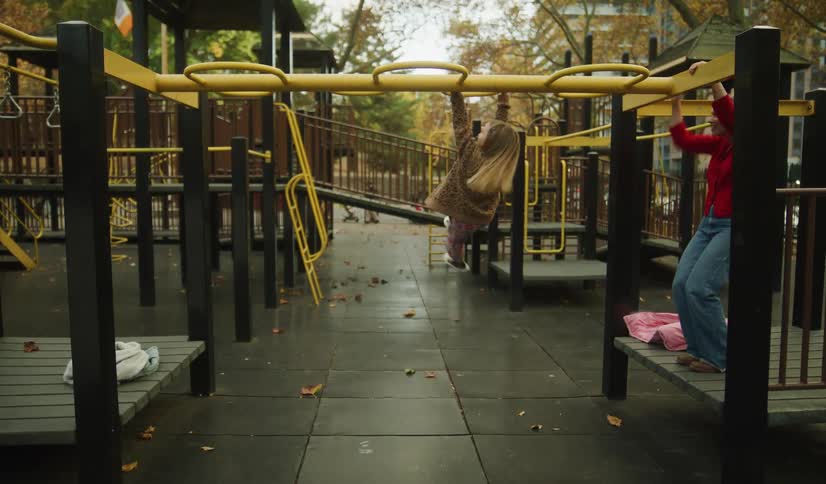 Playful woman and young girl take turns swinging on the monkey bars together at a quiet park playground