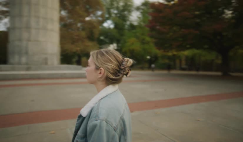 A mother and daughter hold hands while walking through an autumn park before the camera focuses on the mother's contemplative face