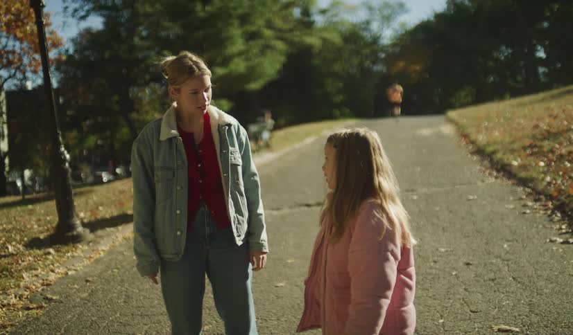 A young woman and a little girl walk hand-in-hand through a sunny park before the girl runs off after an emotional conversation