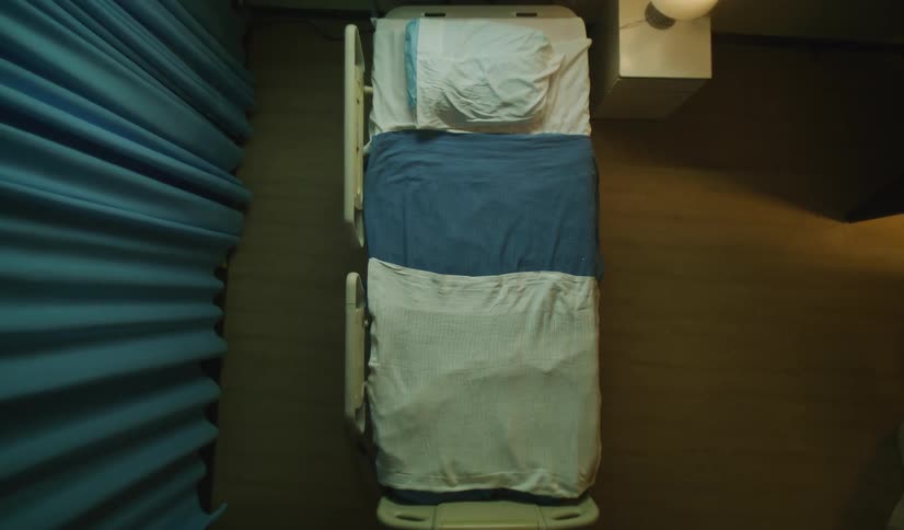 A sterile, empty hospital bed is shown from a top-down perspective in a dimly lit room