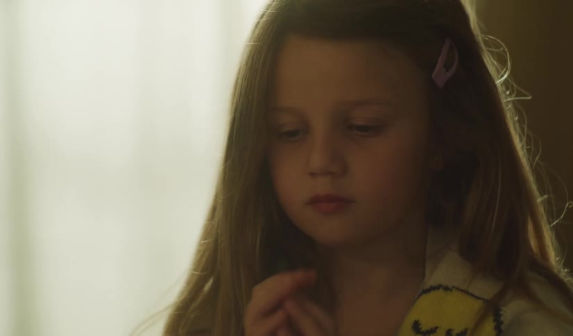 A close-up shot of a young girl with a sad and pensive expression, holding her hands together in thought