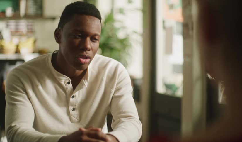 A young Black man listens intently and talks expressively during an intimate conversation with a woman in a cafe