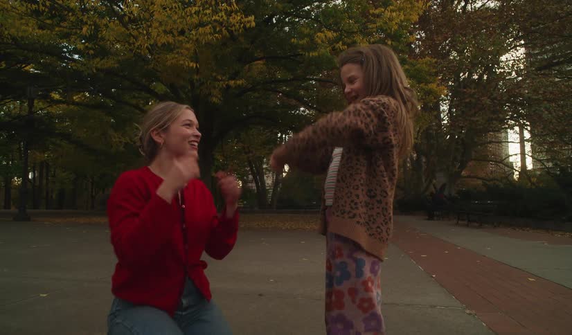 A joyful mother and her young daughter laugh and bond while playing a hand-clapping game together in a city park in slow motion
