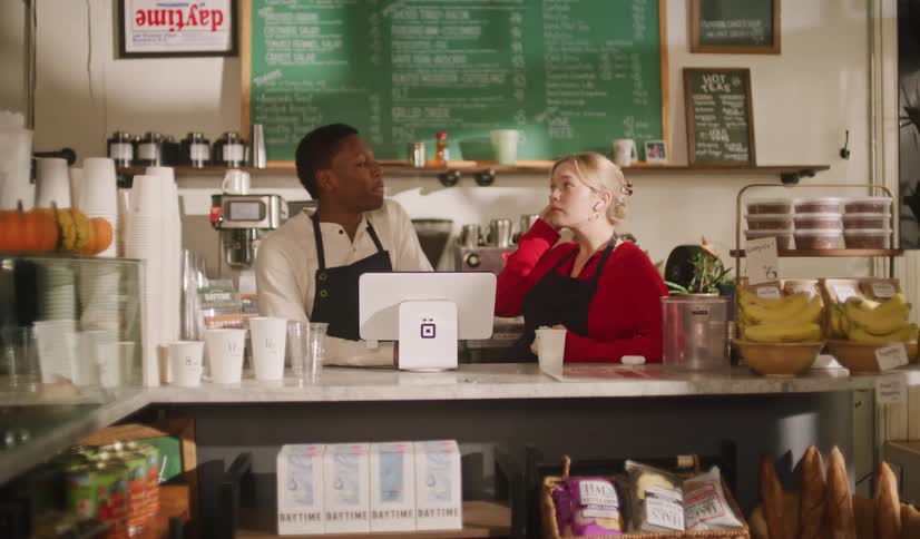 A female barista shows her male coworker a card trick behind the counter of a cozy cafe