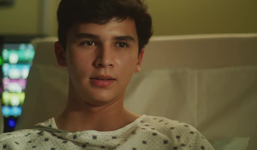 Close up of a teenage boy in a hospital gown talking and smiling while recovering in his hospital bed
