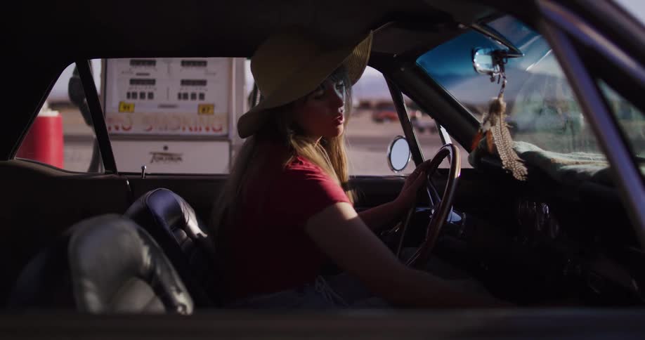A woman on a road trip in her classic muscle car pulls into a vintage roadside gas station in the desert