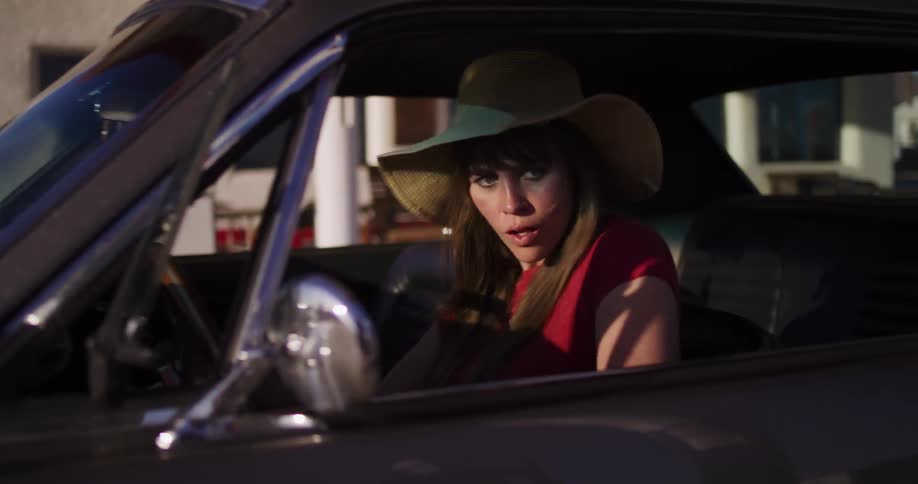 A young woman in a straw hat struggles to start her vintage car, getting increasingly frustrated before finally giving up and exiting the vehicle