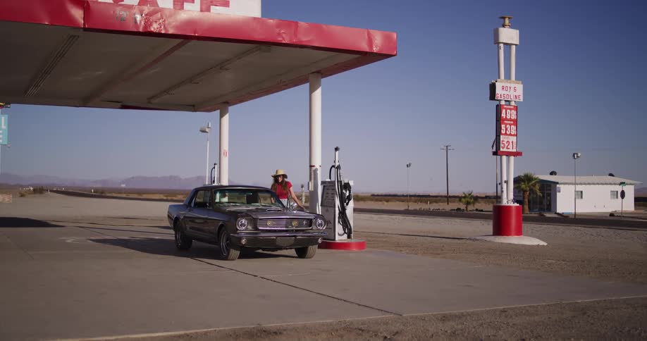 A woman on a road trip gets out of her classic muscle car to pump gas at a remote station in the desert