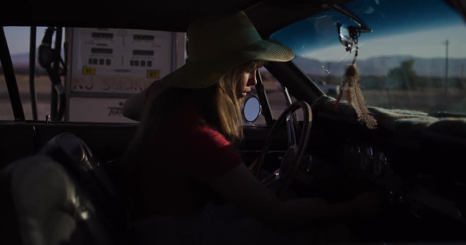 A stylish woman fuels up her vintage muscle car at a remote desert gas station before driving off on a road trip