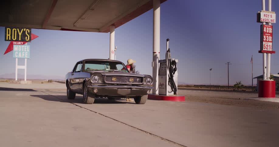 A woman fuels up her classic American muscle car at a retro desert gas station on a sunny day