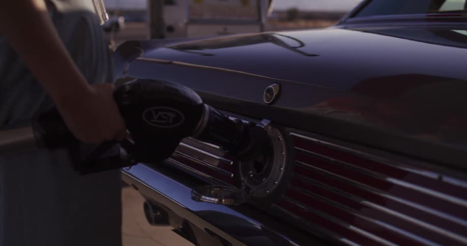 A woman on a road trip stops to refuel her classic vintage car at a remote desert gas station in slow motion