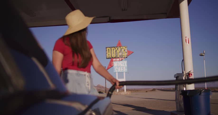 A woman on a road trip stops to pump gas at a retro station in the desert with a vintage sign in the background