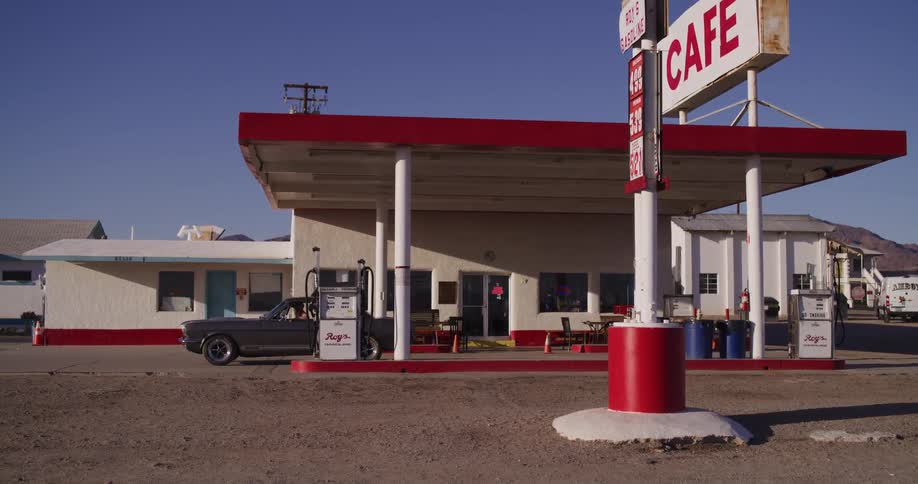 A woman finishes pumping gas into her classic Mustang at a retro desert gas station and cafe before driving away