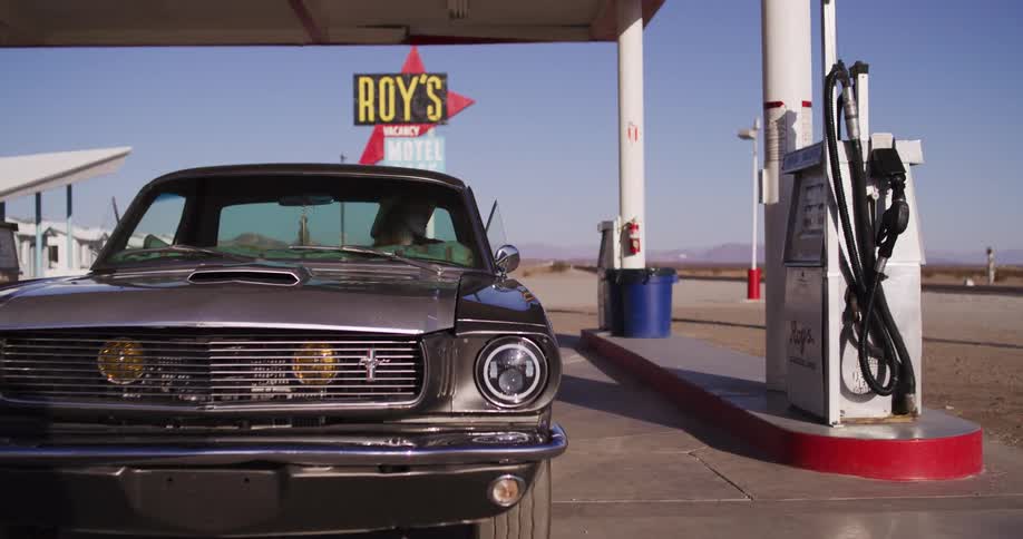 A woman in a classic Ford Mustang pulls into the iconic Roy's Motel Cafe gas station on Route 66 to refuel her car in the desert