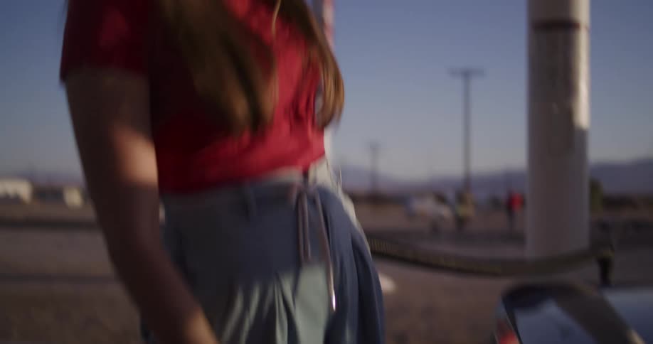 A stylish woman in a sun hat refuels her vintage car at a remote desert gas station during a beautiful golden hour sunset