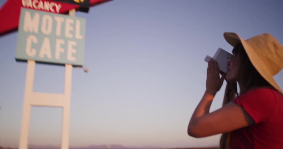 A woman with a vintage camera takes a photo of an iconic roadside motel sign in the desert at dusk