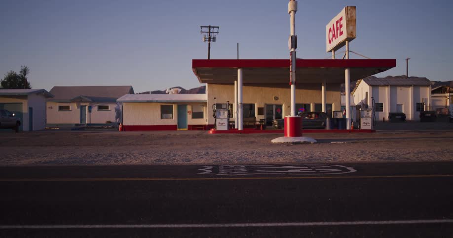 A classic car pulls up to a vintage roadside gas station and cafe on historic Route 66 in the desert