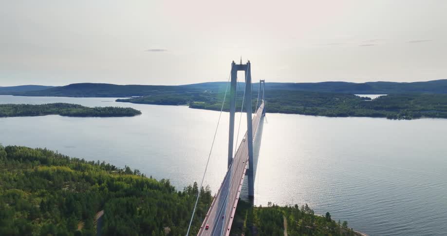 A stunning aerial view shows traffic crossing the iconic High Coast Bridge in Sweden as it spans a wide river amidst a forested landscape