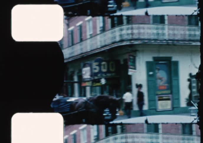 Vintage 1960s film shows a horse-drawn carriage on a bustling Bourbon Street in the French Quarter of New Orleans