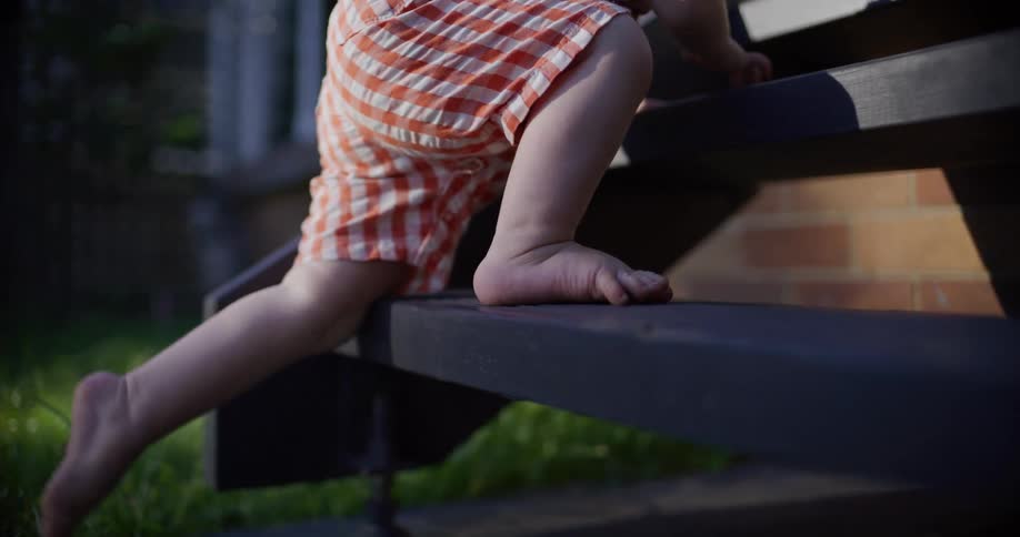 Close up in slow motion of a barefoot toddler's legs and feet as they carefully climb up a set of stairs outdoors