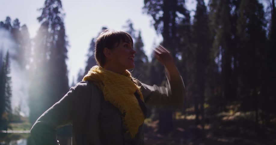 Awe-struck woman yells in excitement as she raises her arm in a beautiful, sun-drenched forest