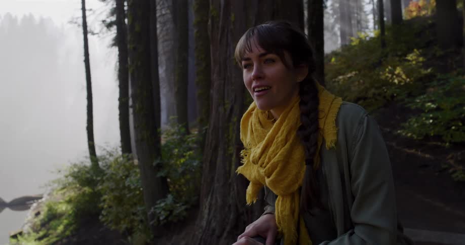 An adventurous young woman stops in awe while hiking up a trail in a foggy forest, captivated by the majestic natural beauty