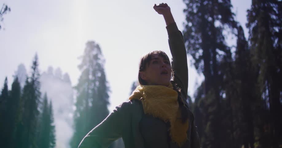 An adventurous woman runs to a scenic viewpoint in a sun-drenched forest, triumphantly raising her fist before taking a photo