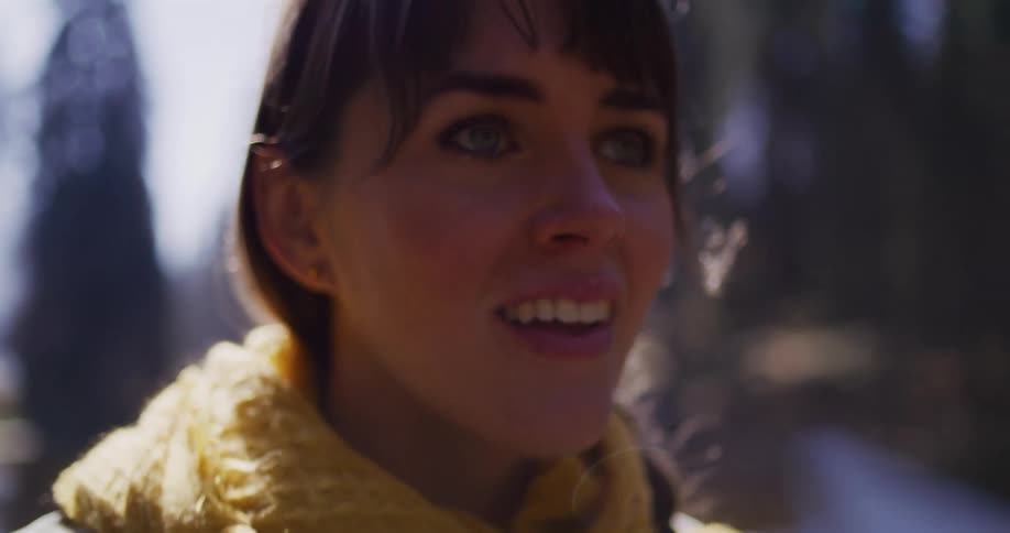A close-up of a smiling woman as she lifts an instant camera to take a photo in a sun-dappled forest