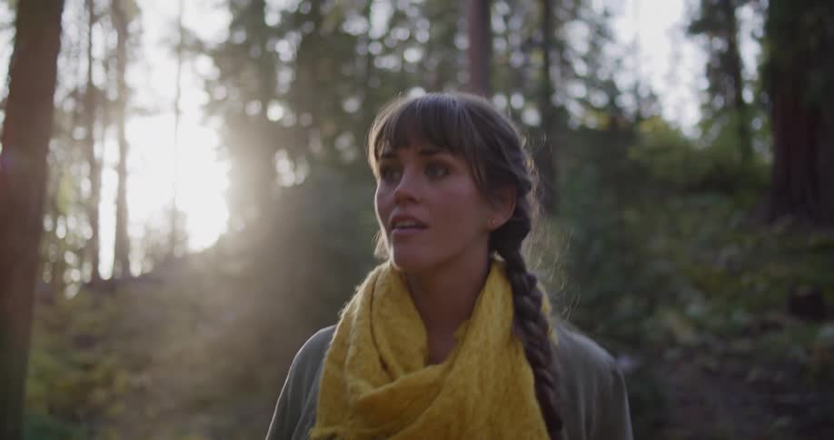 A young woman's expression shifts from joyful wonder to awe-struck surprise as she looks up at the sky in a sunlit forest