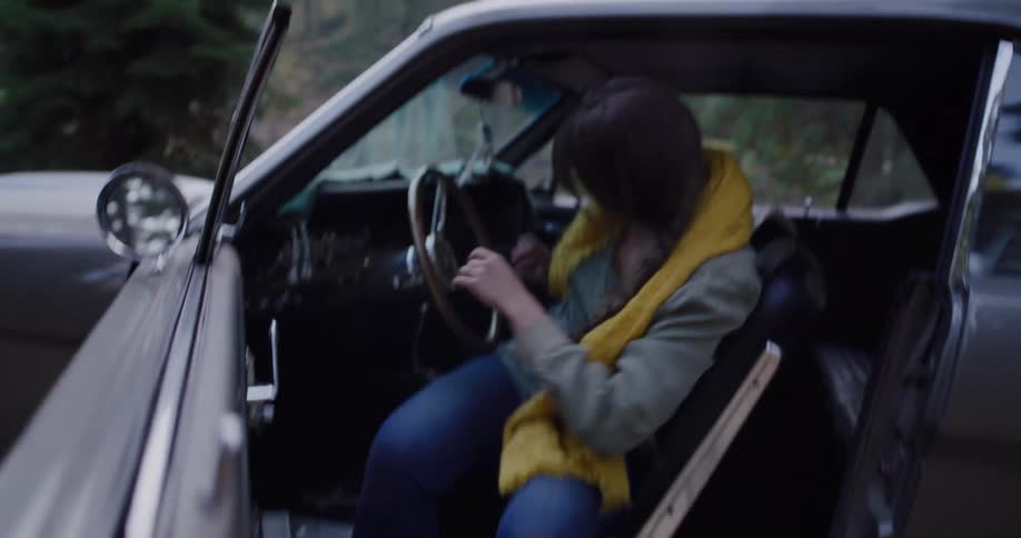 A young woman ties her hiking boots, grabs her instant camera, and excitedly gets out of her classic car for a forest adventure