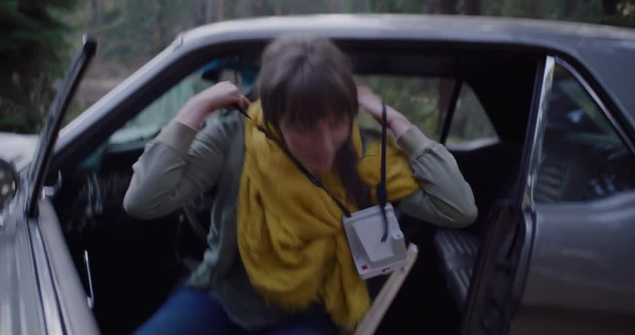 A young woman ties her hiking boots, grabs her instant camera, and gets out of her classic car, ready for a forest adventure