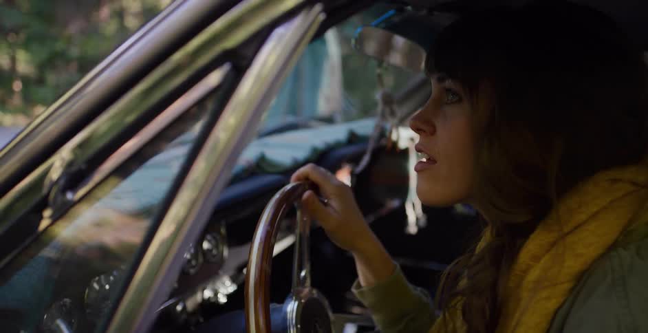 A stylish woman with a yellow scarf drives a classic car through the woods on a road trip