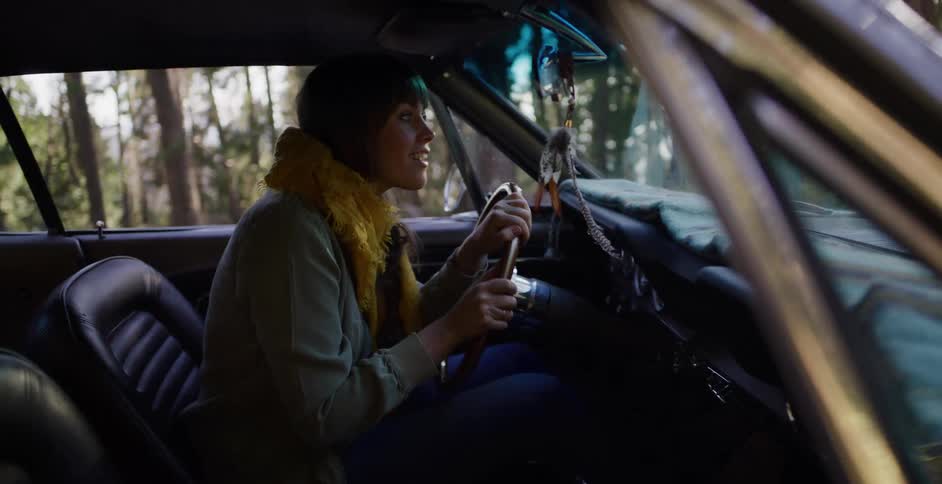 A young woman enjoys a scenic drive through a sunny forest in her vintage muscle car