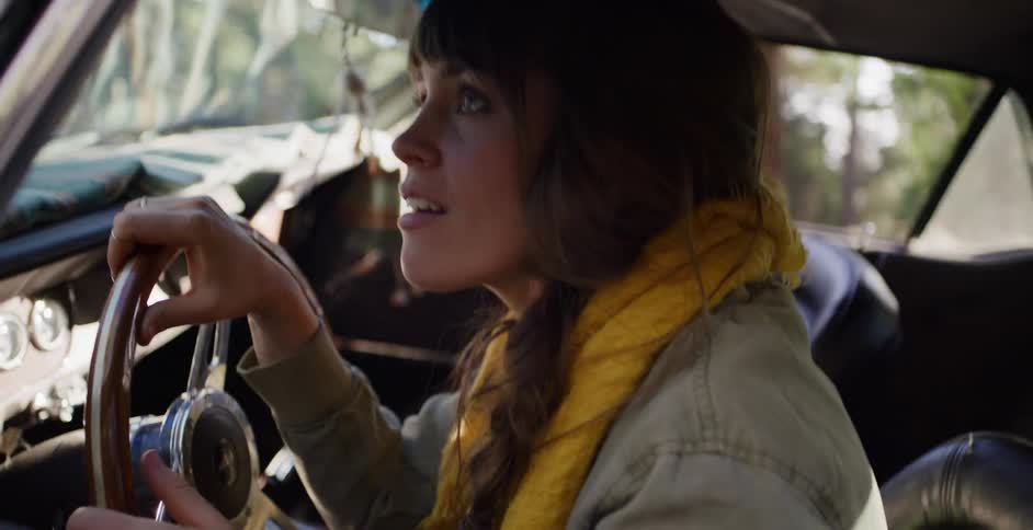Close-up profile of an adventurous young woman driving a classic car through a sun-dappled forest in slow motion