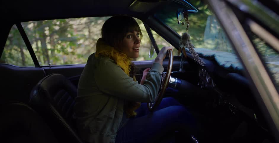 Frightened woman in a vintage car looks over her shoulder in terror while stopped on a remote forest road