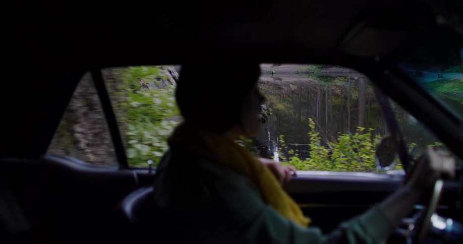 A woman in a vintage car takes a scenic drive through a tranquil forest, passing a reflective lake
