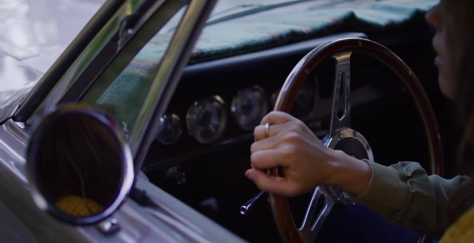 Close up of a woman's hands on the steering wheel of a classic convertible car