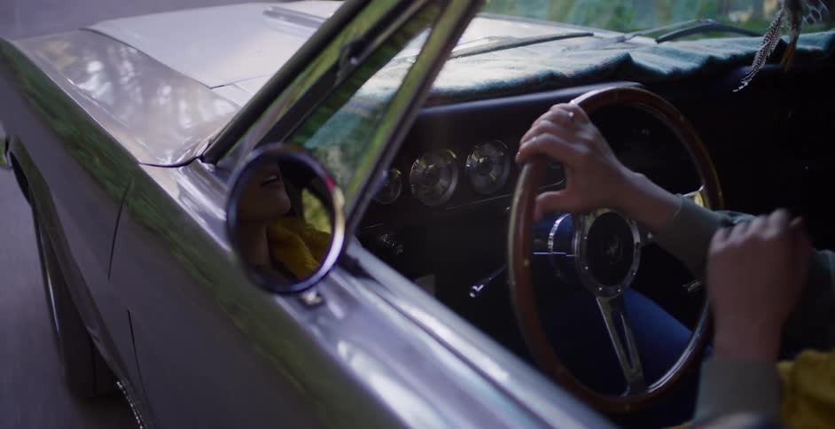 Adventurous woman enjoys a scenic drive in a vintage car, her joyful reflection seen in the side mirror amidst sun flares
