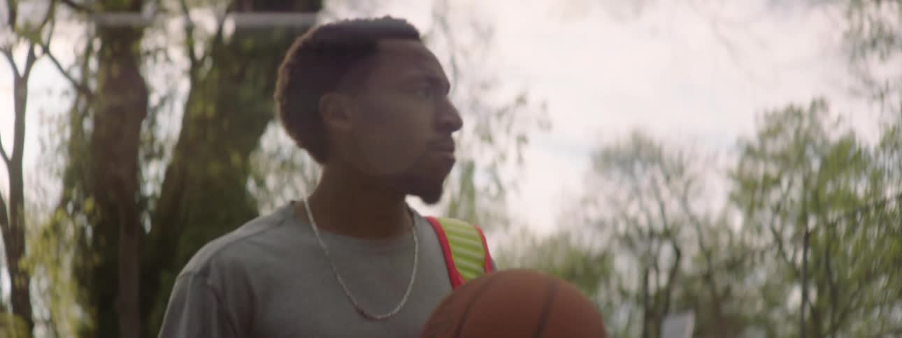 Slow motion close-up of a focused young man walking through a sun-drenched park with his basketball