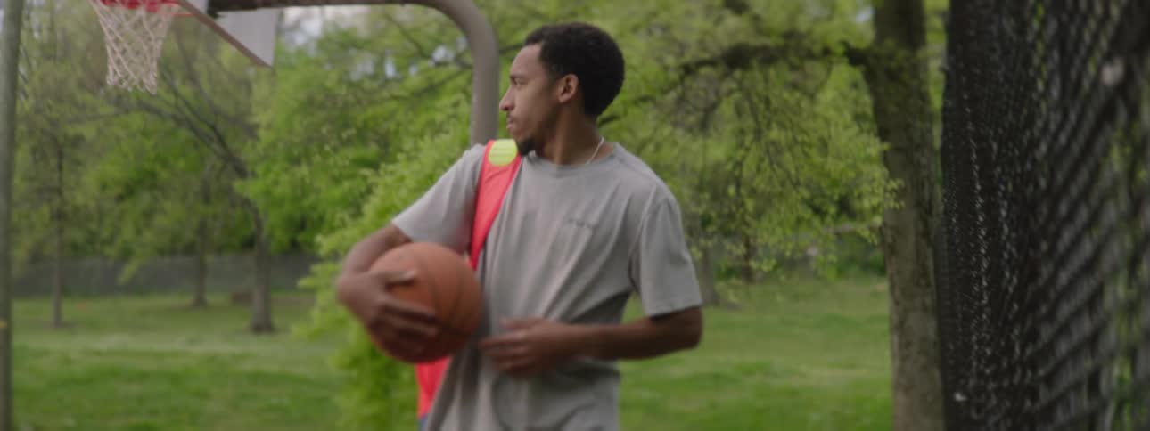 A young man grabs his colorful backpack and basketball and walks off an outdoor court in slow motion